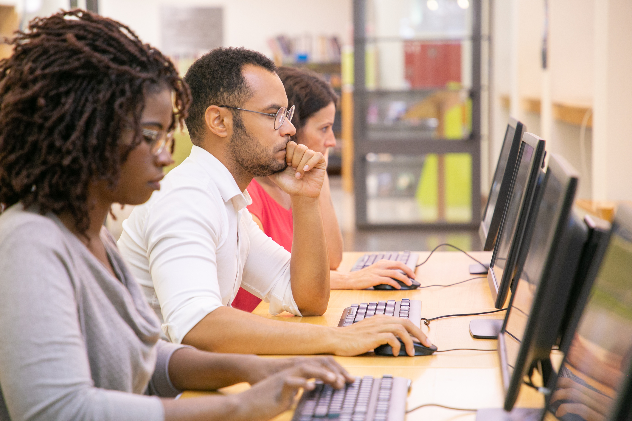 Two women and a man sit at computers.  