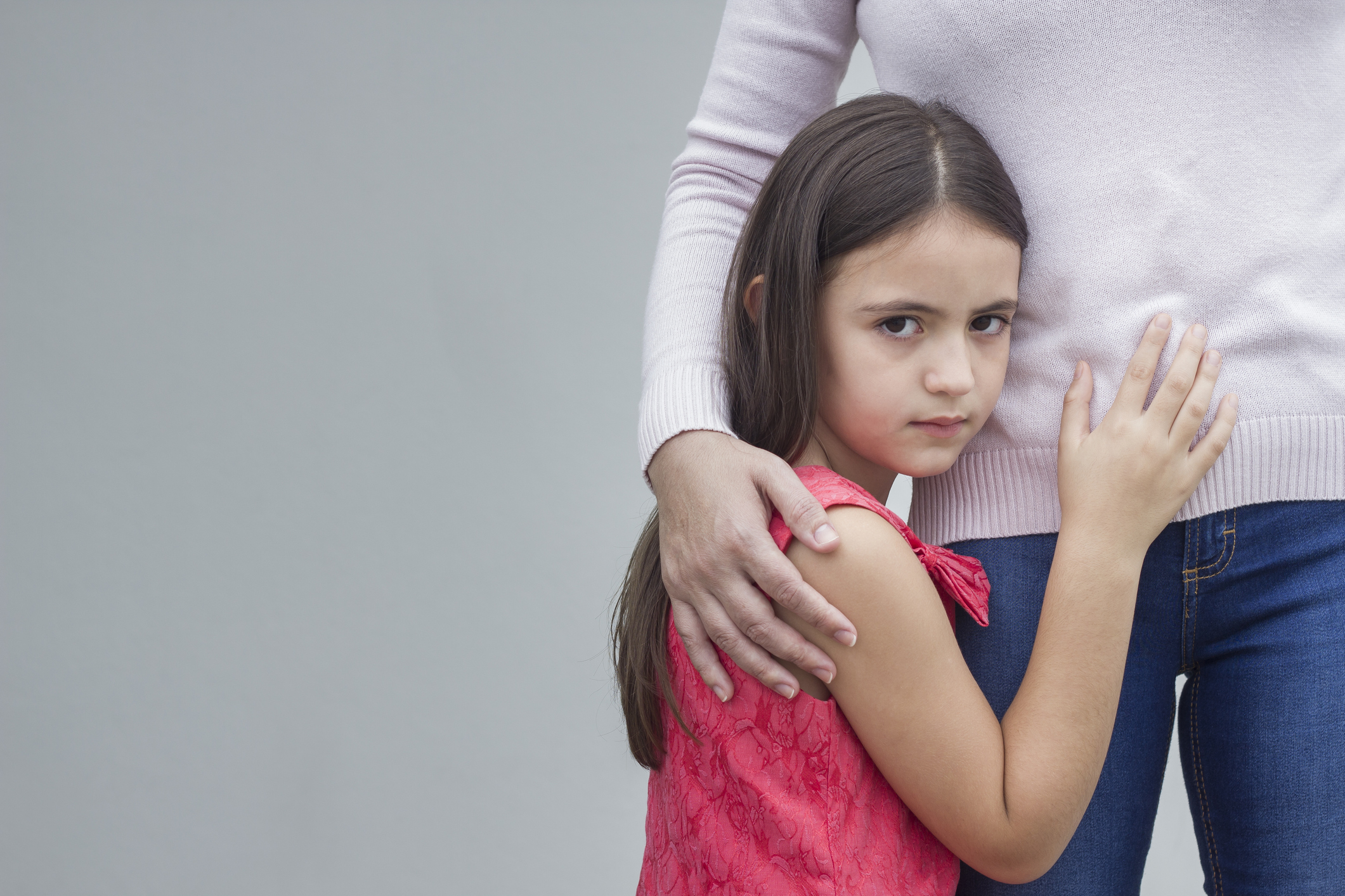 Young girl faces camera, hugs woman at waist